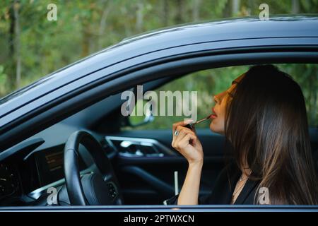 Konzentrierte Frau, die Lippenstift ansetzte, während sie im Auto saß Stockfoto