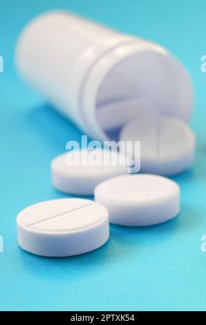 Mehrere weiße Tabletten fallen aus der Kunststoffbehälter auf der blauen Fläche. Hintergrundbild über medizinische und pharmazeutische Themen Stockfoto