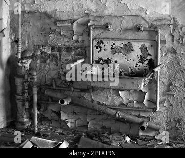 Schwarz-Weiß-Aufnahme von rostigem Becken und Rohren in einem verlassenen Gebäude. Stockfoto