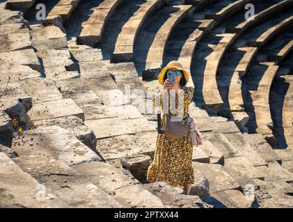 Eine vietnamesische Asiatin macht ein Foto mit ihrem Mobiltelefon, während sie das große römische Amphitheater in Side in der Provinz Antalya, Türkei (Tur Stockfoto