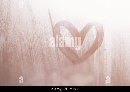 Eine herzförmige Zeichnung durch einen Finger auf einen Beschlagenen Glas im regnerischen Wetter gezeichnet Stockfoto