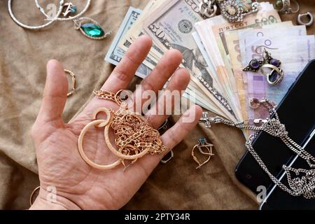 Marodeuter reichen mit einem Haufen gestohlener Schmuckstücke, Geld und Smartphones auf einem Militäruniform-Stoff. Plünderung durch russische Soldaten in der ukrainischen citi Stockfoto