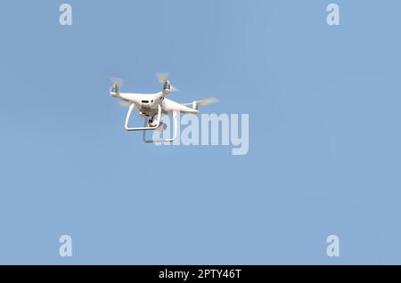 Big White drone schwebt in einem hellen wolkenlosen blauen Himmel, Radio Control Helicopter mit tragbaren Videokamera Versorgung Stockfoto