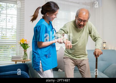 Junge Frau helfen orthopädischen Patienten zu helfen, mit Gehstock zu Hause aufstehen, Pflege Krankenschwester hilft älteren behinderten Mann zu stehen mit Stockfoto
