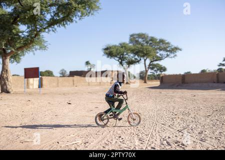 Ein kleiner Junge fährt mit dem Fahrrad auf einer Sandstraße in seinem Dorf in der ländlichen Region Segou in Mali, Westafrika. 2022 Dürre und Hungerkrise in Mali. Stockfoto