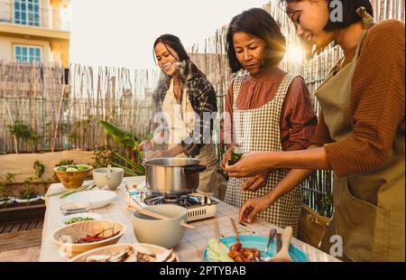 Südostasiatische Mutter und ihre Töchter haben Spaß dabei, gemeinsam auf der Terrasse des Hauses ein Rezept zuzubereiten Stockfoto