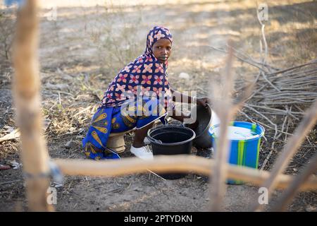 Eine Fulani-Frau mit sauberen weißen Schuhen und traditionellem Kleid wäscht Geschirr vor ihrem Wohngebiet in der Region Segou, Mali, Westafrika. 2022 Dürre und Hungerkrise in Mali. Stockfoto