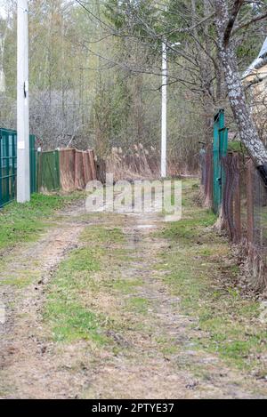 Straße auf dem Land, wackelige Zäune und Betonbeleuchtungsmasten. Ländlich, Garten, Land. Stockfoto