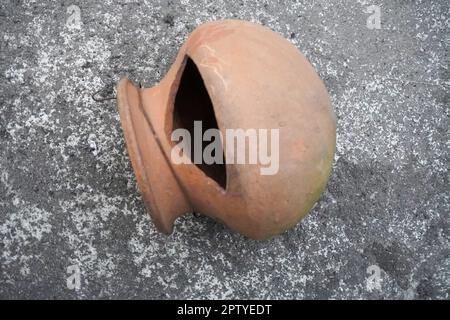 Alte, leere runde, rote Tonschüssel. Runde Tonschale. Draufsicht auf Tonschale auf Bodenhintergrund. Tonschüsseln auf Betonboden Stockfoto