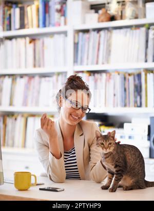 Mein kleiner Furball. Eine attraktive junge Frau, die mit ihrer Katze kuschelt, während sie von zu Hause aus arbeitet Stockfoto