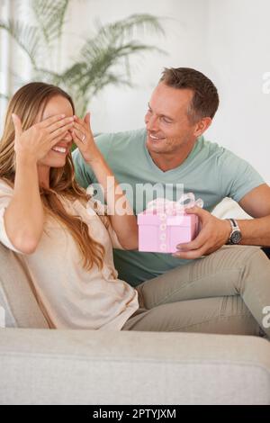 Okay, ich werde nicht hinsehen. Ein gutaussehender Mann, der seine Frau mit einem Geschenk überraschte Stockfoto