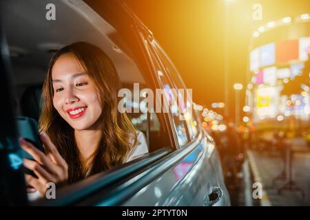Asiatische Geschäftsfrau arbeitet spät pendeln aus dem Büro in Taxi Rücksitz mit Handy in der Stadt in der Nacht nach der späten Arbeit, Happy Beautiful Woman Text Stockfoto