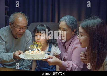 Glückliche asiatische Familie Großeltern und Mutter feiern genießen Geburtstagsfeier mit Kuchen der Enkelin weht Kerze zu Hause in der Nacht, Geburtstag Stockfoto