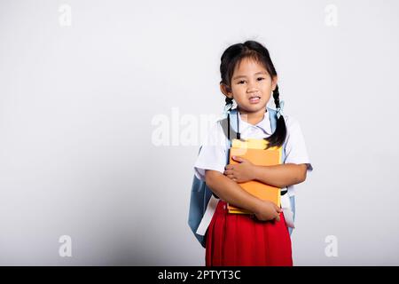 Asiatische liebenswert Kleinkind lächelnd glücklich tragen Student thai uniform roten Rock stehen halten oder umarmende Buch im Studio geschossen isoliert auf weißem Hintergrund, Portr Stockfoto