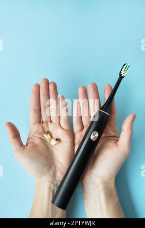 Eine moderne elektrische Zahnbürste in der einen Hand und Zähne in der anderen Hand auf blauem Hintergrund. Die Zahnextraktionsoperation. Der Begriff Hygiene f Stockfoto