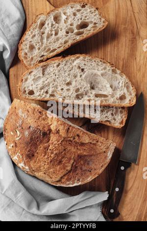 Geschnittener Laib mit kunstvollem Sauerteigbrot auf einem Schneidebrett. Draufsicht, vertikaler Rahmen Stockfoto