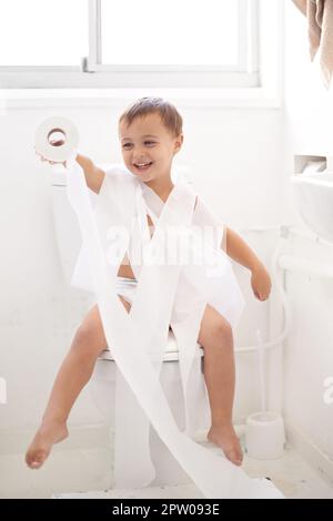 Töpfchentraining kann eine Herausforderung sein... humorvolle Aufnahme eines kleinen Jungen, der auf einer Toilette sitzt und in Toilettenpapier eingewickelt ist Stockfoto