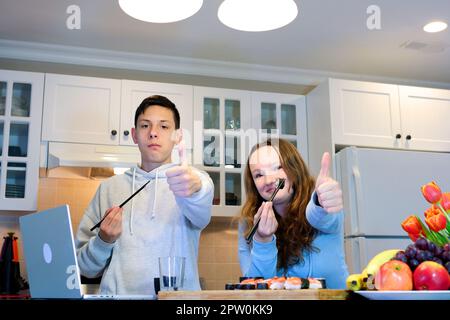 Sushi zusammen essen. Wunderschönes Paar, das Sushi isst, während es auf der Couch nebeneinander sitzt Stockfoto