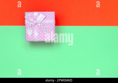 Kleine rosa Geschenkkarton liegen auf Textur Hintergrund der Mode pastell Farben Türkis und Rot Papier in minimalen Begriff. Stockfoto