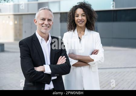 Geschäftsmann mit Geschäftsfrau, die draußen steht. Zwei Führungskräfte mit verschränkten Armen starrten draußen in die Kamera. Stockfoto