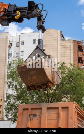 Hydraulikbagger bewegt sich bei Aushub- und Restaurierungsarbeiten auf Stadtstraßen mit Sicherheitsrechnung im Bau und setzt Erde in Lkw frei Stockfoto