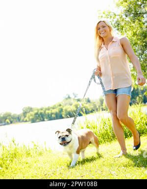 Wir gehen jeden Tag spazieren. Eine schöne Blondine, die mit ihrem Hund spazieren geht Stockfoto