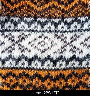 Ein Teil eines Ornaments auf einem Wollpullover. Wintermotive. Beige, braune, weiße, schwarze Fäden zum Handstricken. Strickmuster. Rhombusch Stockfoto