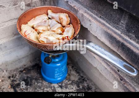 Spanische Mahlzeit im Freien. Frisch gebratene Hähnchenflügel auf einer Pfanne in einem Campinggasofen Stockfoto