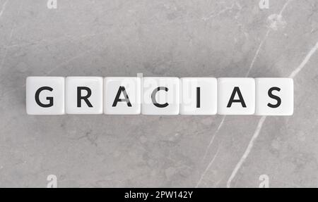 Dankeswort auf weißen Blöcken in spanischer Sprache auf grauem Marmorhintergrund. Gracias Worthintergrund Stockfoto