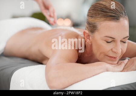 Der Körper verdient es, mit Freundlichkeit behandelt zu werden. Eine Masseurin gießt Peeling Salz auf den Rücken eines Kunden Stockfoto