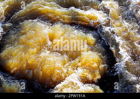 Das schräge Sonnenlicht scheint durch das sprudelnde Wasser eines Flusses mit Stromschnellen Stockfoto