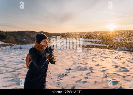 An einem sonnigen Winterabend bläst eine Frau Schnee aus ihren Palmen. Stockfoto