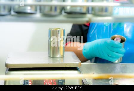 Sardines cans weigh on a weight scale by worker. Worker working in canned food factory. Food industry. Canned fish factory.  Worker in food processing Stock Photo