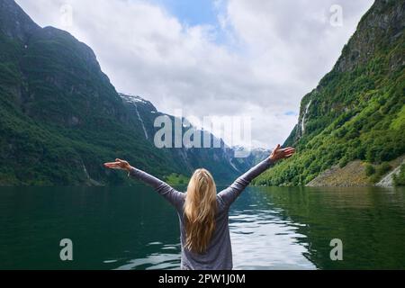 Reise-Adventure-Frau feiert die erhobenen Arme beim Blick auf den majestätischen Fjordsee des Gletschertals auf Entdeckungsreise Entdecken Sie die wunderschöne Erde. Stockfoto