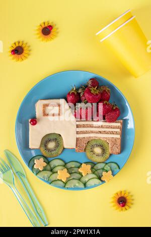 Gesunder Toast für Kinder in Form eines Autos mit Erdbeeren, Kiwi und Käse auf blauem Teller auf gelbem Hintergrund, Draufsicht Stockfoto