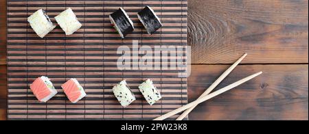 Sushi rollen und liegen auf einem hölzernen Eßstäbchen Bambus Stroh serwing Mat. Traditionelle asiatische Lebensmittel. Ansicht von oben. Stockfoto