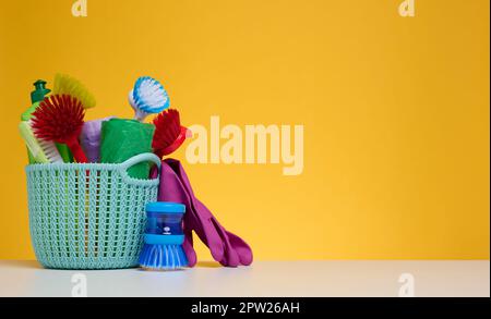 Kunststoffkorb mit Bürsten, Desinfektionsmittel in einer Flasche, Gummihandschuhe auf gelbem Hintergrund. Hausreinigungsgegenstände, Kopierraum Stockfoto