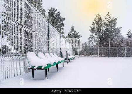 Die Reihe leerer grüner Kunststoffsitze auf dem Sportgelände, die mit Schnee bedeckt sind. Wintersaison. Stockfoto