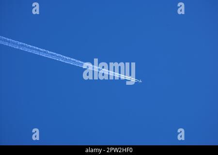 Flugzeug contrail gegen klaren blauen Himmel Hintergrund mit Copyspace. Blick auf ein entferntes Passagierflugzeug, das in großer Höhe am blauen Himmel abfliegt Stockfoto