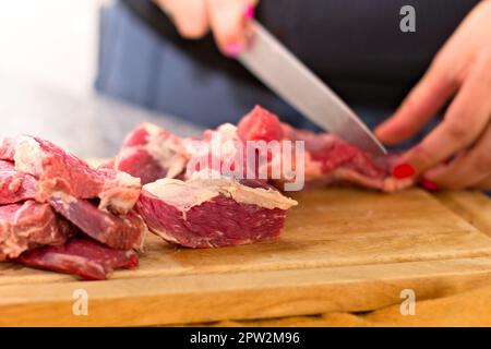 Frau schneidet Fleisch auf einem hölzernen Schneidebrett. Nahaufnahme. Stockfoto