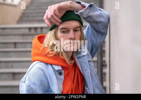 Ein aufgebrachter Millennials-Typ, der sich an eine Betonwand lehnte, während er auf einer Fußgängertreppe stand Stockfoto