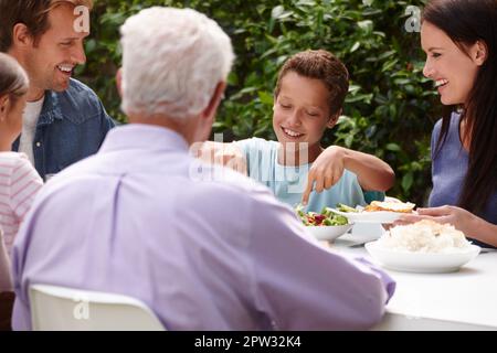 Lass uns essen. Eine glückliche, generationsübergreifende Familie, die draußen zusammen zu Abend isst Stockfoto