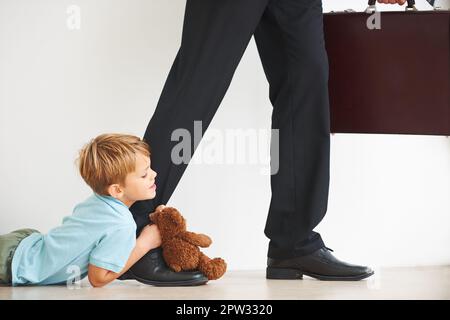 Nein, geh nicht. Ein kleiner Junge auf dem Boden, sehr unglücklich, dass sein Faher zur Arbeit geht Stockfoto