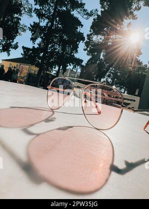 Die Sonne scheint durch die Sonnenbrille, die auf dem Tisch liegt und einen Schatten wirft Stockfoto