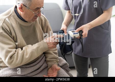 Junge Frau Ärztin trägt weiße Uniform mit Stethoskop überprüfen reifen Patienten Blutdruck bei der Besprechung im Krankenhaus, ernsthaften Arzt gp verwenden Stockfoto
