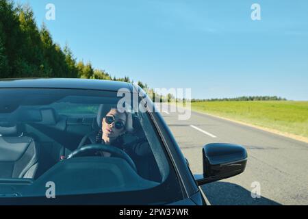 Hübsche Frau, die auf einer Landstraße ein kraftvolles Auto fährt Stockfoto