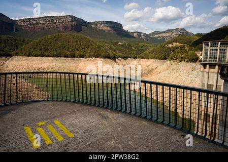 Vilanova de Sau, Spanien - 27. April 2023: Der Damm am Sau-Wasserreservoir. Die Wasserreservoirs, eine der wichtigsten Wasserquellen der spanischen Region Katalonien und insbesondere der Stadt Barcelona, sind nach Angaben der katalanischen Wasserbehörde zu 6 % ausgelastet, während die Wasserreservoirs der Region zu 27 % ausgelastet sind. Die die lokale Regierung gezwungen hat, Maßnahmen gegen die Wasserknappheit zu ergreifen, da Spanien in eine Phase der chronischen Dürre eingetreten ist. Der rekordverdächtige Tiefstand hat die Stadt Sant Romà mit ihrem berühmten Glockenturm wieder auftauchen lassen, der in den 60s Jahren, als der Damm überflutet wurde, überflutet wurde Stockfoto