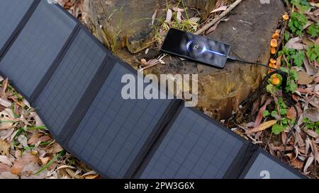 Tragbares Solarpanel-Lade-Smartphone über Mehrzweckkabel, Powerbank, Uhren, Laptops mit Naturhintergrund. Saubere Energie für Camping oder ein Stockfoto