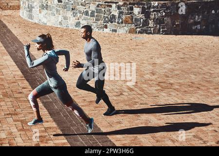 Partner in Bewegung und im Leben. Aufnahme von zwei jungen und sportlichen jungen Menschen, die durch die Stadt laufen. Stockfoto