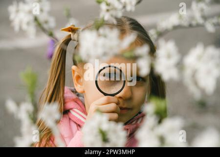 Kind lernt etwas über die Umwelt. Naturerziehungsaktivität für den Welt-Erde-Tag. Im Frühling auf Erkundungstour, blühende Blumen im Garten. Ein ernstes Mädchen Stockfoto